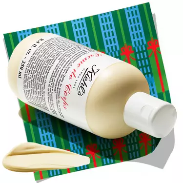 Bottle of Kiehl's Creme de Corps body lotion with a dollop of cream, resting on a patterned holiday background.​