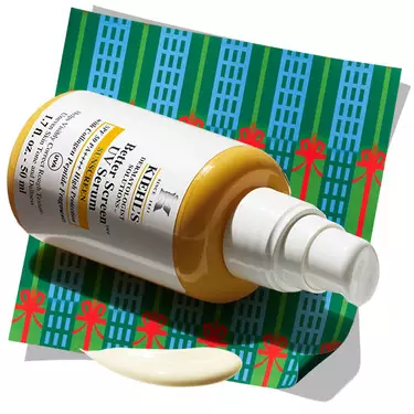 Kiehl's Better Screen UV Serum bottle with a dollop of serum, resting on a patterned holiday background.​